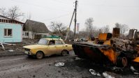 Local resident drives past a destroyed Russian armoured personal carrier in the village of Nova Basan